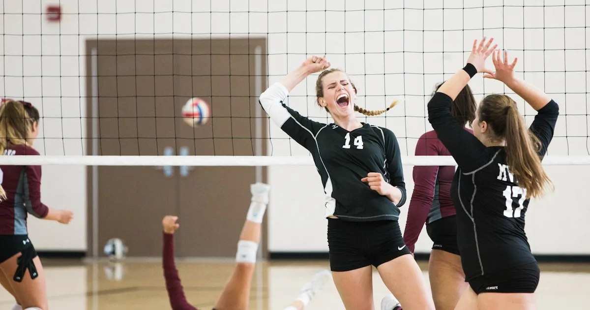 Time de vôlei escolar comemorando ponto no ginásio com uniformes numerados